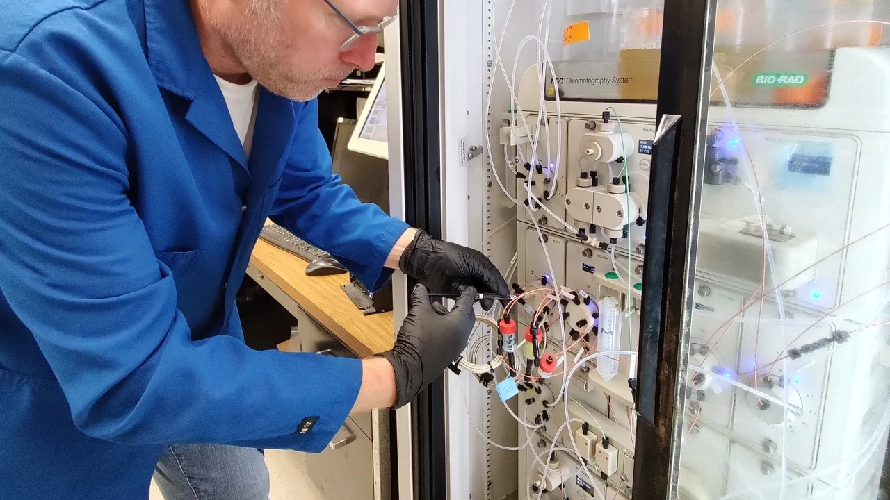 Scientist wearing mask and gloves working with a chromatography system in a laboratory.