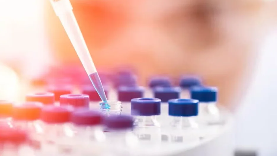 Scientist using a pipette to place liquid into vials with blue caps in a lab.