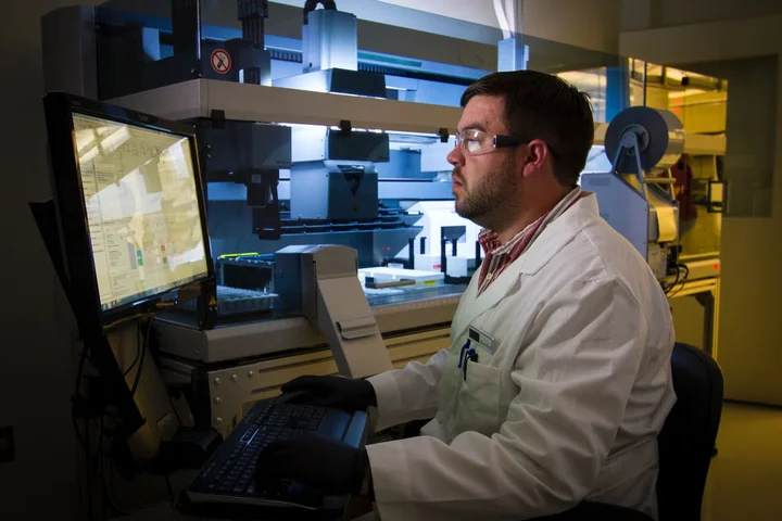 Scientist in lab coat operating laboratory automation equipment using a computer workstation.