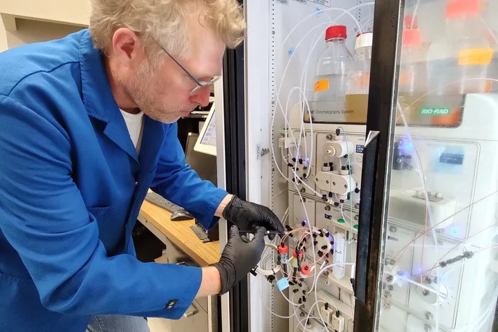 Scientist wearing mask and gloves working with a chromatography system in a laboratory.