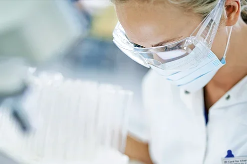 A scientist wearing a mask and goggles studies test tubes. 