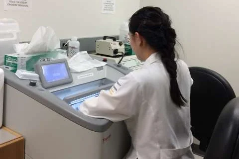 Scientist using a cryostat machine to prepare frozen tissue samples in a lab setting.