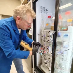 Scientist wearing mask and gloves working with a chromatography system in a laboratory.